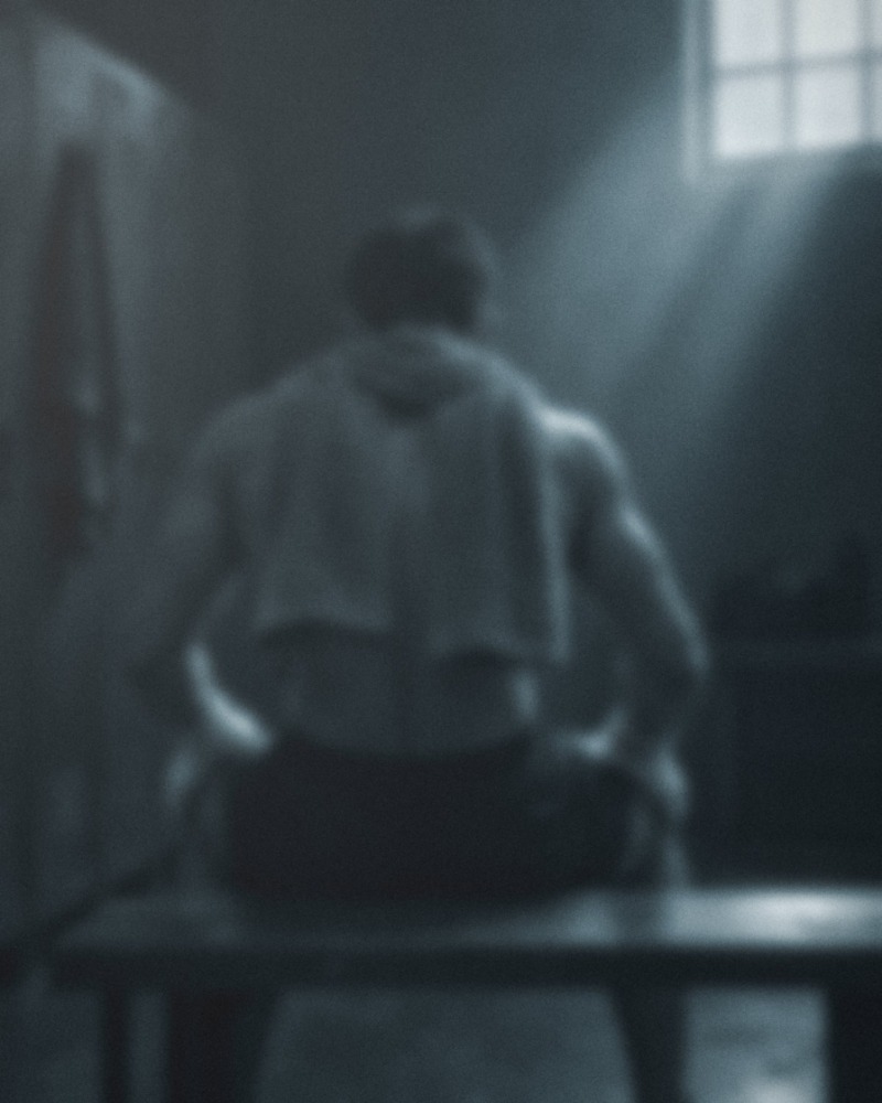 A fighter on a locker-room bench, back to camera, a towel across his shoulders, seen out of focus.